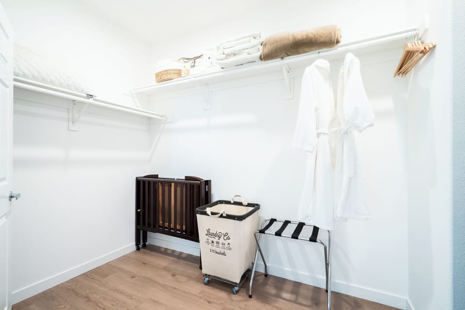 Primary walk in closet offering a crib, laundry basket, luggage rack and robes.