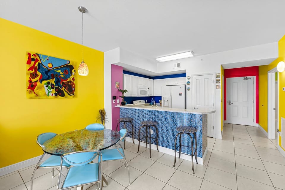 Modern kitchen and dining area with colorful walls and a glass table.