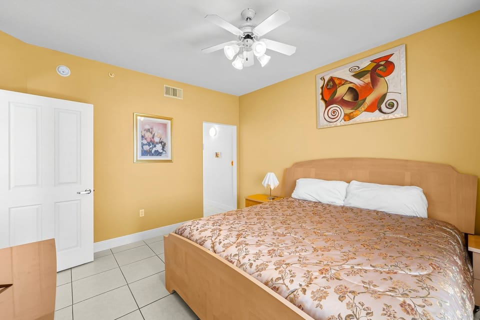 Cozy bedroom with a ceiling fan and warm yellow walls featuring modern artwork.