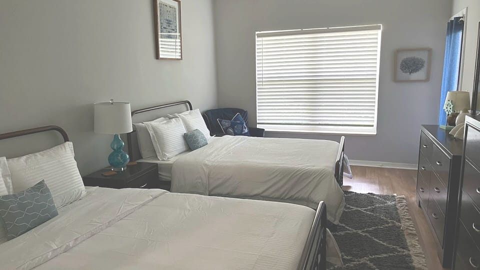 Comfortable bedroom with two beds, dresser storage, natural light, and soft neutral finishes.