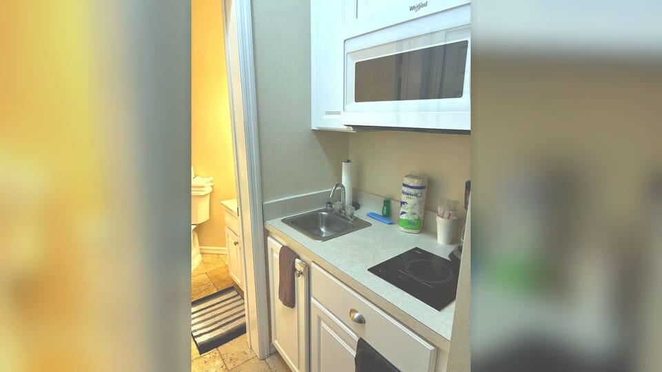 Convenient kitchenette area with sink, microwave, mini fridge, and easy access to the bathroom.