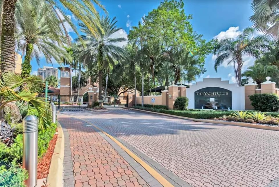 Gated community entrance framed by tropical trees and elegant pavers