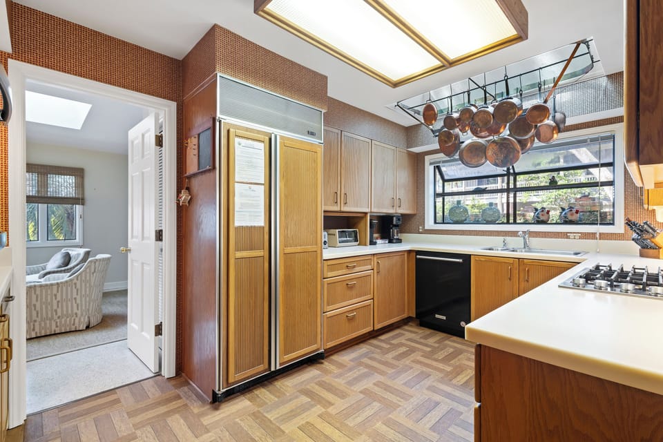 This cozy kitchen features warm wood cabinetry, a unique pot rack centerpiece, and a large window that fills the space with natural light.