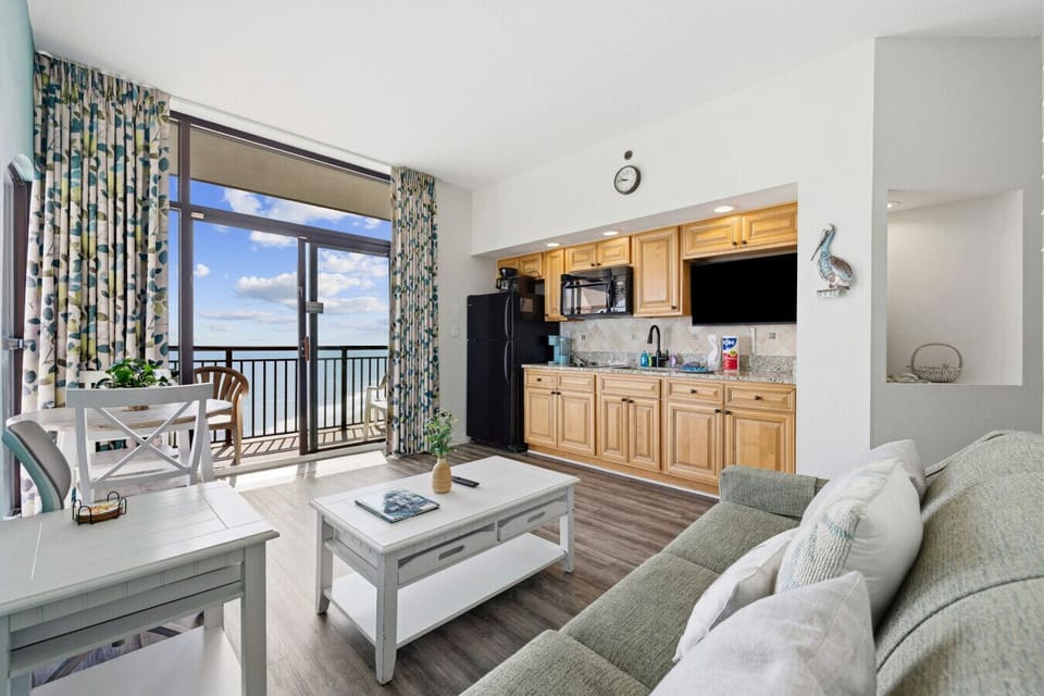Open kitchen and living area with floor-to-ceiling windows, abundant natural light, and a fully stocked kitchen with all major appliances and Keurig. Relax on a full-sized couch with a smart TV for entertainment.