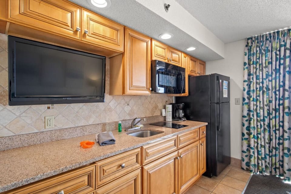 Clean, modern kitchen fully stocked for family meals, featuring a refrigerator, microwave, sink, and 2-burner stovetop. Includes cookware, dinnerware, and a Smart TV—perfect for preparing and serving vacation dinners in Myrtle Beach.