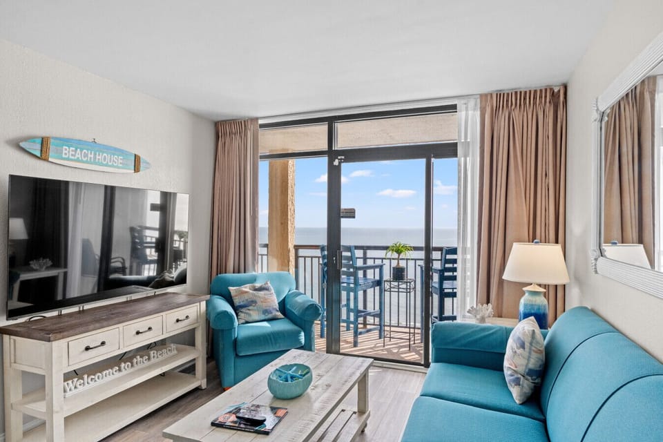 Oceanfront living room with comfortable seating for five, a 65” Vizio Smart TV, and direct balcony access. The perfect space to start your morning with ocean views or unwind with a cozy vacation movie night.