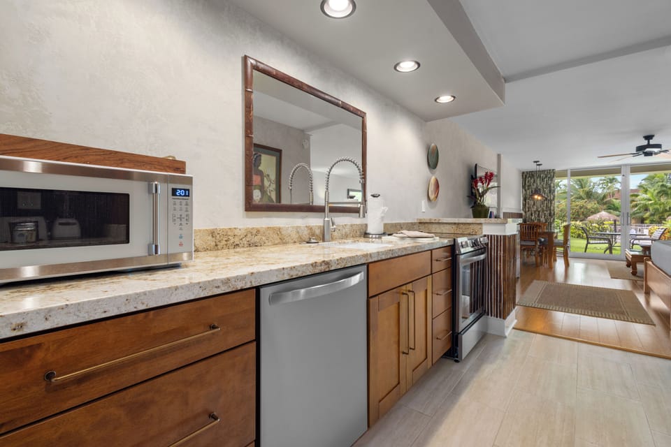 Step into your bright, open kitchen where cooking becomes a pleasure. Gleaming granite counters, stainless appliances, and warm wood cabinetry invite you to create memorable meals while tropical views beckon beyond.