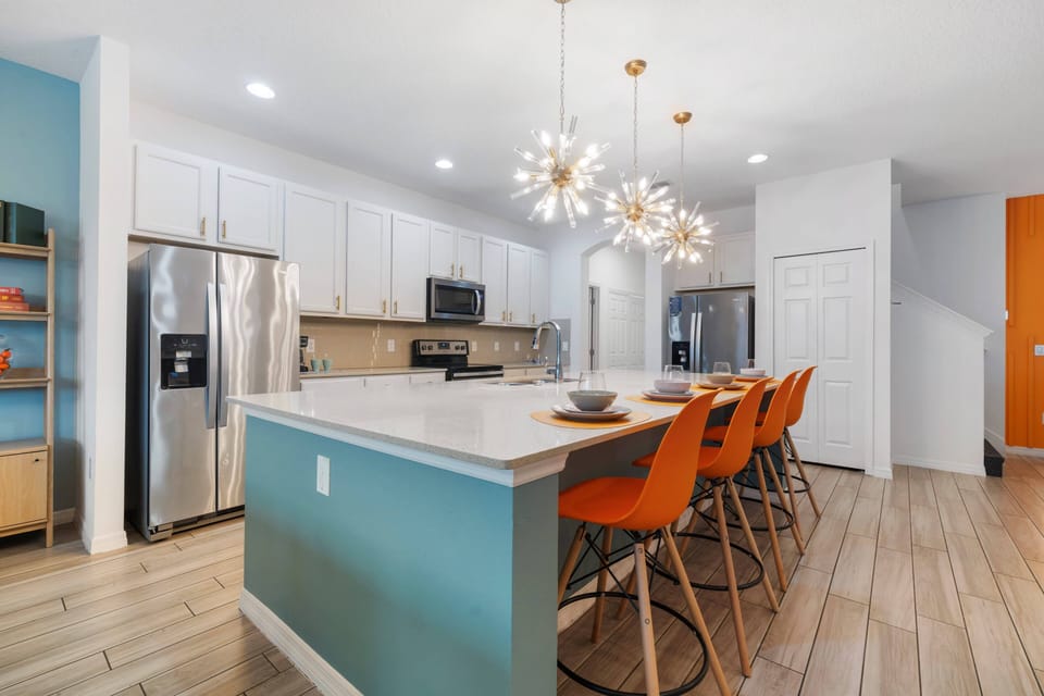 - Modern kitchen with quartz island and bright pendant lights  
- Orange bar stools add playful charm to the cooking space  
- Stainless steel appliances make family dining convenient