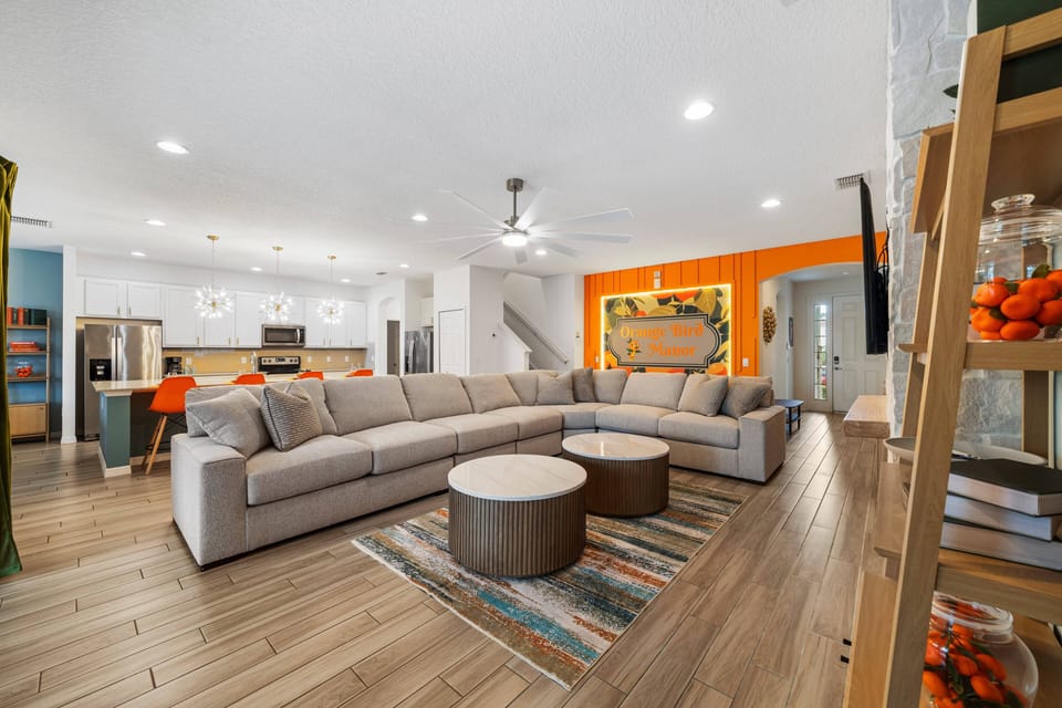 - Spacious living room with sectional seating and modern décor  
- Open floor plan connects to kitchen and dining for family ease  
- Orange Bird Manor sign adds playful charm to the cozy lounge