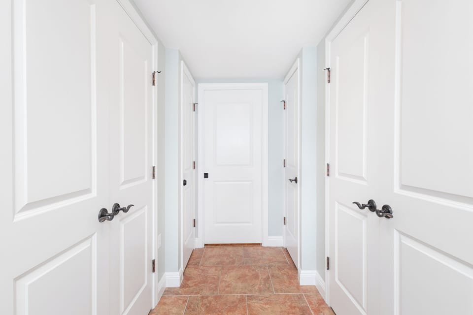 Multiple doorways guide you through this elegant, light-filled hallway with crisp white finishes and warm terracotta flooring underfoot.