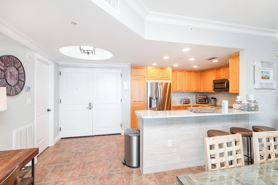 Step into your bright, open living space featuring a fully equipped kitchen with modern appliances, breakfast bar seating, and vaulted ceilings that create an airy, welcoming atmosphere for your stay.
