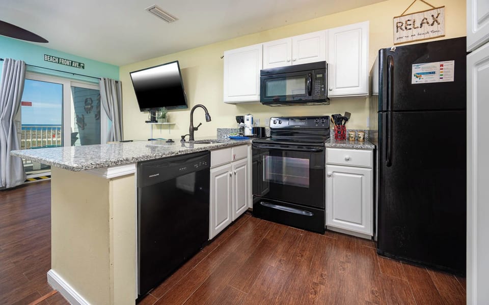 This kitchen features sleek black appliances, granite countertops, and a beach view, perfect for enjoying meals together