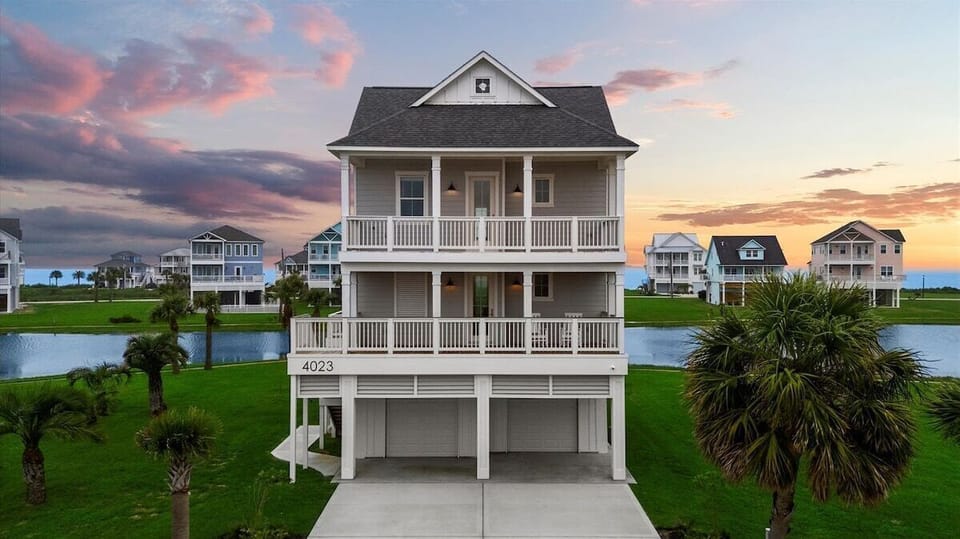 Stunning elevated coastal beach house exterior in Galveston, TX with spacious driveway, modern architecture, and waterfront community views.