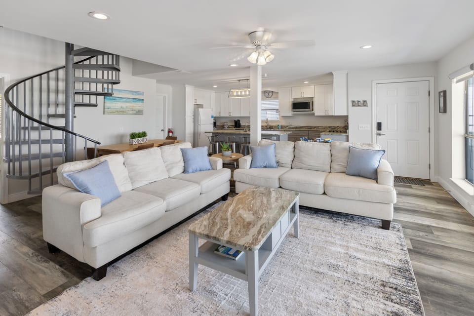 Unwind on plush sofas in your bright, airy living room featuring an open kitchen and elegant spiral staircase.