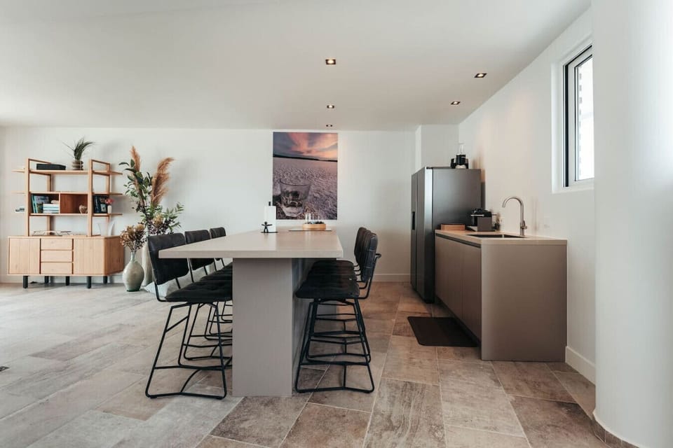 Sleek, modern kitchen and dining area with a long gray island, black bar stools, and a unique salt flat photograph.