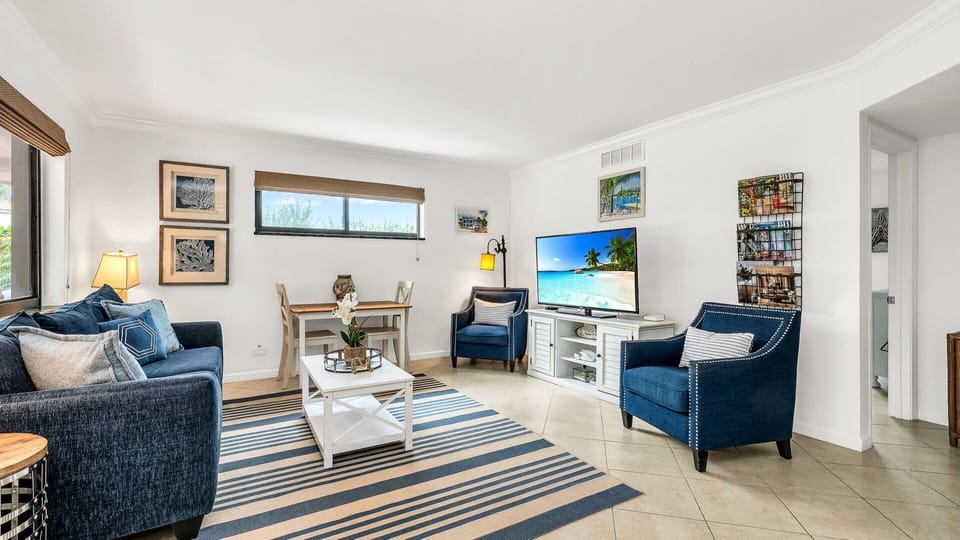 Bright and breezy coastal living room featuring a bold navy sofa, streaming TV, a collection of books, and a charming breakfast nook—perfect for relaxed mornings and cozy evenings.