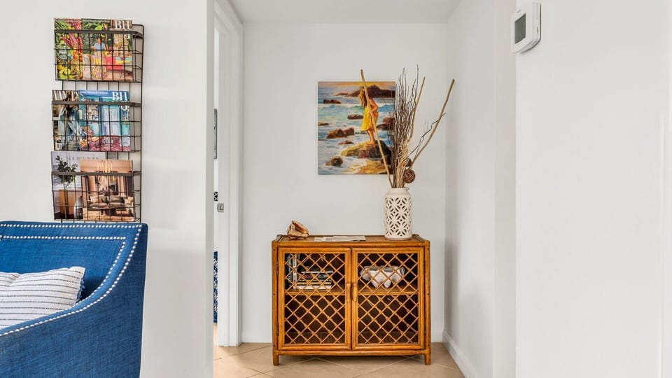 Coastal-inspired reading nook with a rattan cabinet stocked with books, magazines, and local guides—perfect for winding down or planning your next adventure.