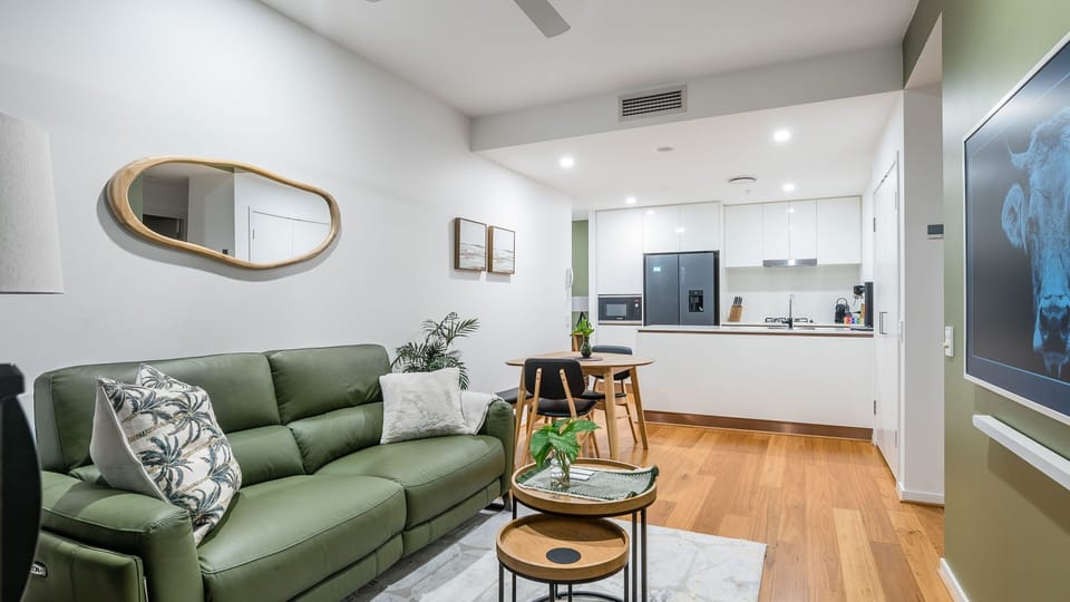 Living Room and Kitchen: Sink into the bespoke olive-green sofa for an evening of relaxation. Your compact but fully-equipped kitchen features high-gloss white cabinetry and all the essentials, including a large black refrigerator.