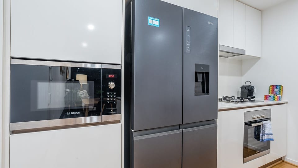 Gourmet Appliances: The kitchen is anchored by a sleek, large black refrigerator with a built-in water/ice dispenser. A microwave is integrated into the surrounding white cabinetry.