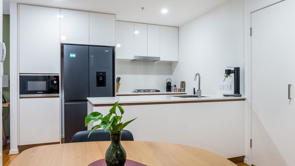 Gourmet Appliances: The kitchen is anchored by a sleek, large black refrigerator with a built-in water/ice dispenser. A microwave is integrated into the surrounding white cabinetry.