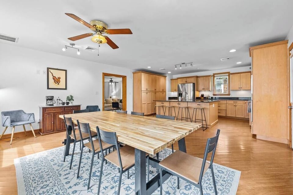 Dining area w/ long table set for group meals beside an open kitchen layout
