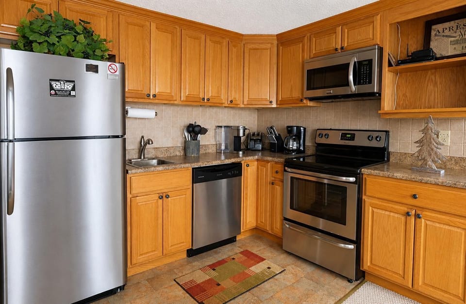 Stainless steel appliances line granite countertops with oak cabinets and beige tile backsplash in the kitchen.