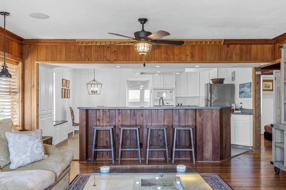 Rustic kitchen bar with wooden stools and a ceiling fan overlooking the living area.