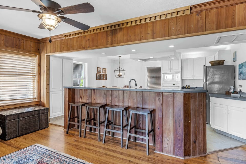 Rustic kitchen bar area with wooden stools and ceiling fan for casual dining.