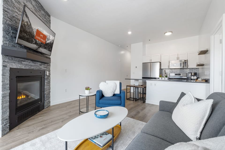 View of couch and TV and fireplace with kitchen in background