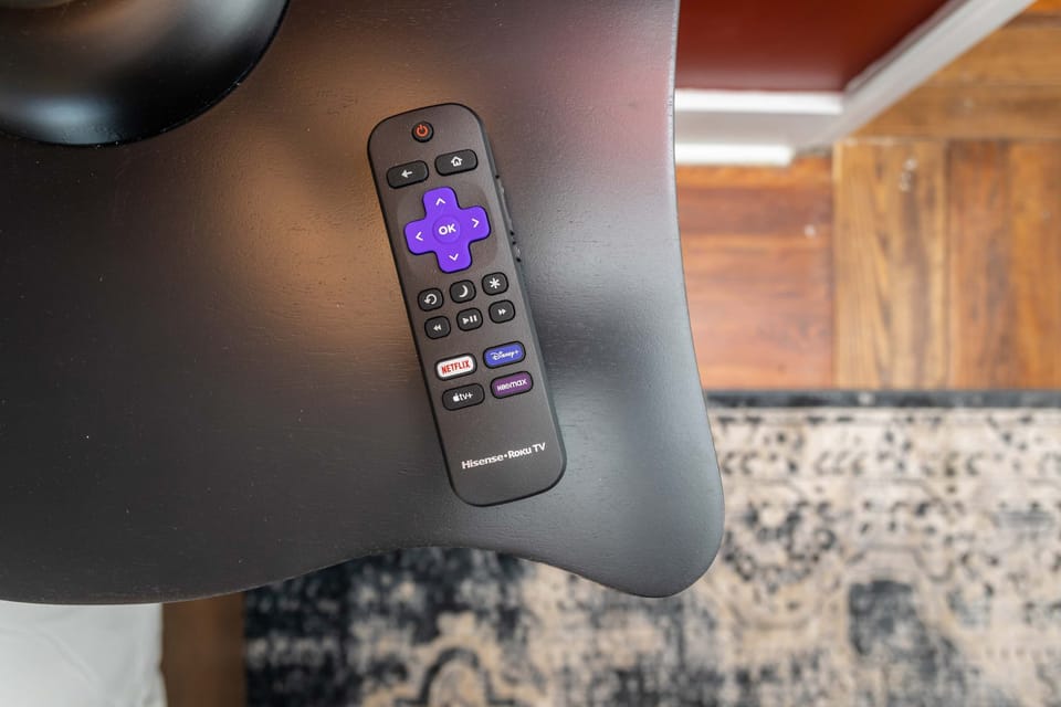Streaming remote control on a black side table with hardwood floor and patterned rug in the background