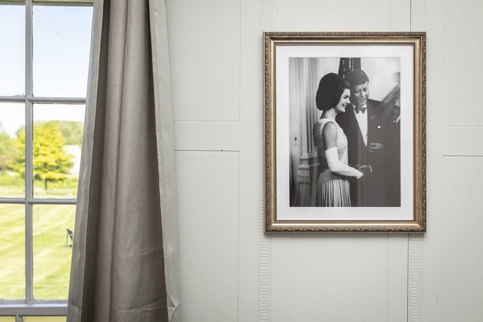 framed black and white photograph displayed on a white wall next to a window with beige curtains