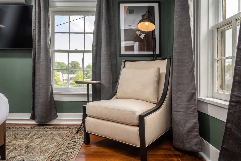 Cozy beige armchair with a reading lamp by windows offering natural light and a view.