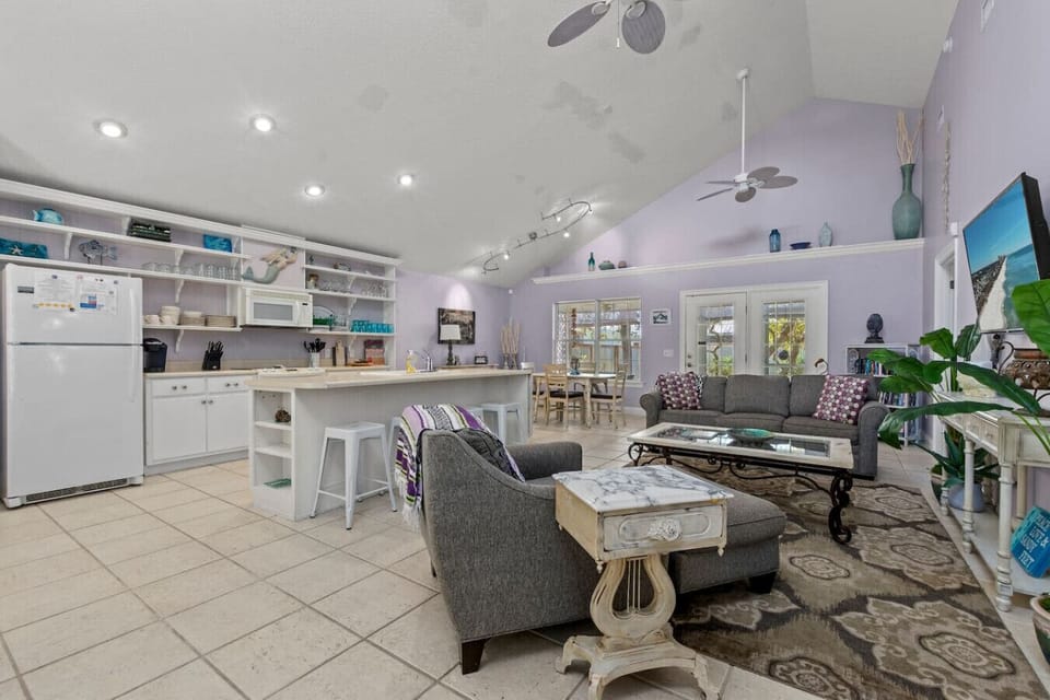 The view of the living, dining, and kitchen areas reveals an open-concept space where comfort and style seamlessly blend. The living room, with its cozy couches and high ceilings, flows effortlessly into the dining area, perfect for family meals or entert