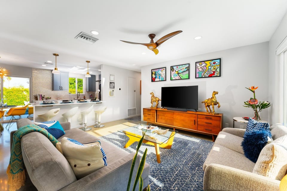 Living space includes a large sofa, flat screen TV and open concept to the Kitchen/Dining Area with views of the backyard through sliding glass doors. 