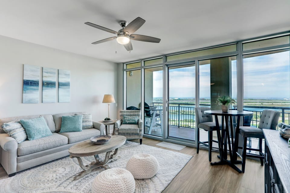 Bright and airy living room with coastal décor, modern furnishings, and stunning floor-to-ceiling views of Galveston Bay. Perfect for relaxing or entertaining.
