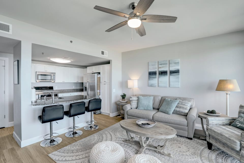 Modern open-concept kitchen and living area with coastal accents, granite countertops, and bar seating—ideal for relaxing or entertaining by the beach.