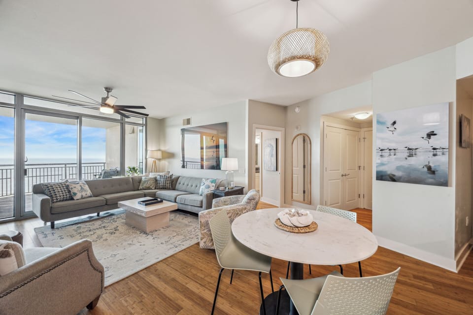 Spacious open-concept living and dining area with stunning Gulf views, modern coastal décor, and access to private balcony.