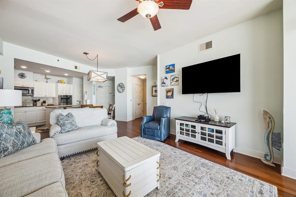 Open living space with flat-screen TV, coastal accents, and rich wood floors—perfect for relaxing after a day on the beach at Palisade Palms.
