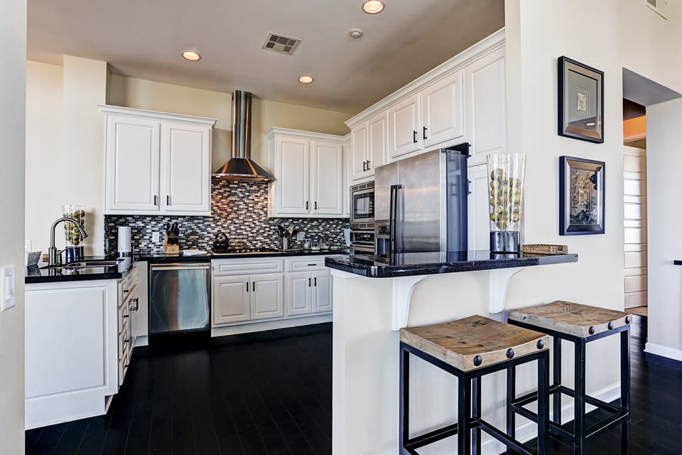 Modern kitchen with stainless steel appliances, sleek black countertops, and a stylish mosaic tile backsplash.