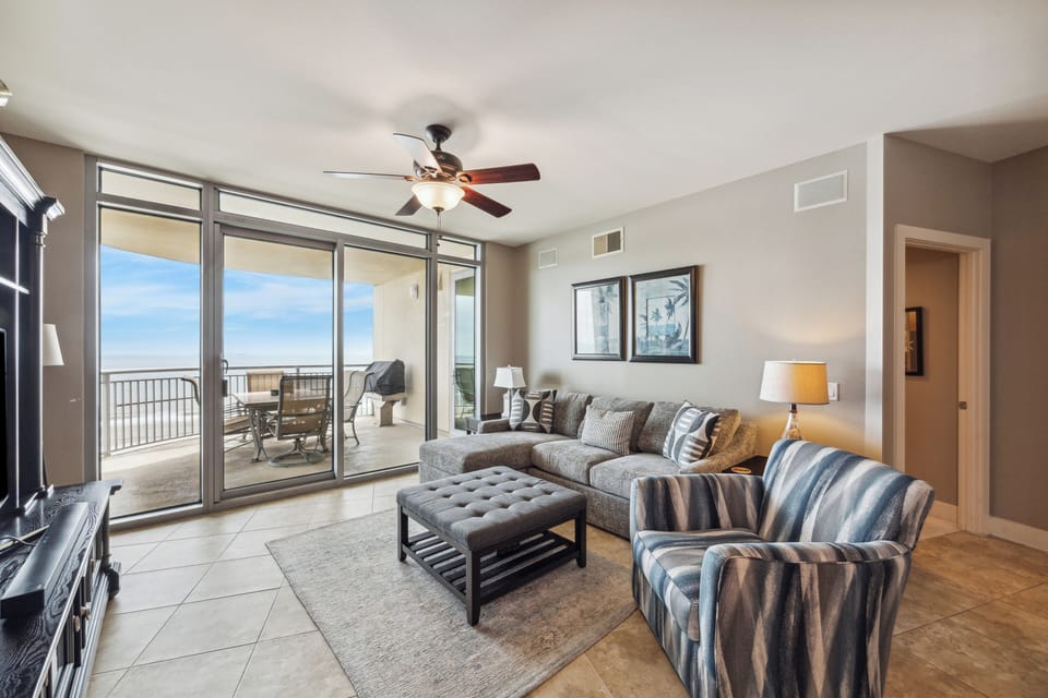 Open-concept living area features floor-to-ceiling glass doors that flood the space with natural light and provide panoramic Gulf views, plus direct access to the oversized balcony.