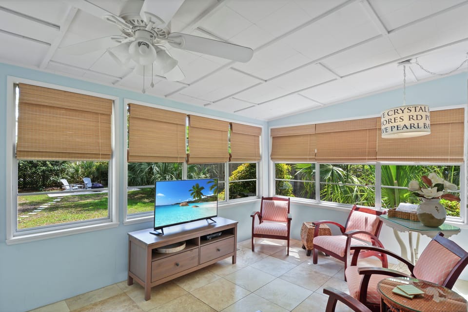 Sunroom TV Lounge with Backyard View - Sunroom seating area with Smart TV, ceiling fan, bamboo shades, and windows facing the yard.