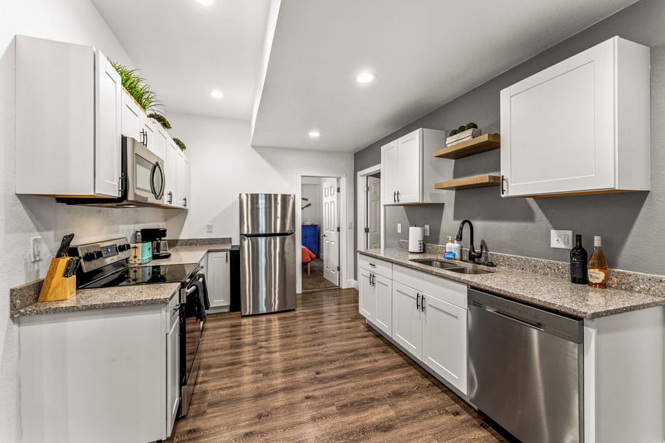 - Fully equipped kitchen with stainless steel appliances and modern finishes
- Plenty of countertop space, white cabinetry, and open shelving for easy cooking
- Warm wood floors and recessed lighting add charm and functionality

