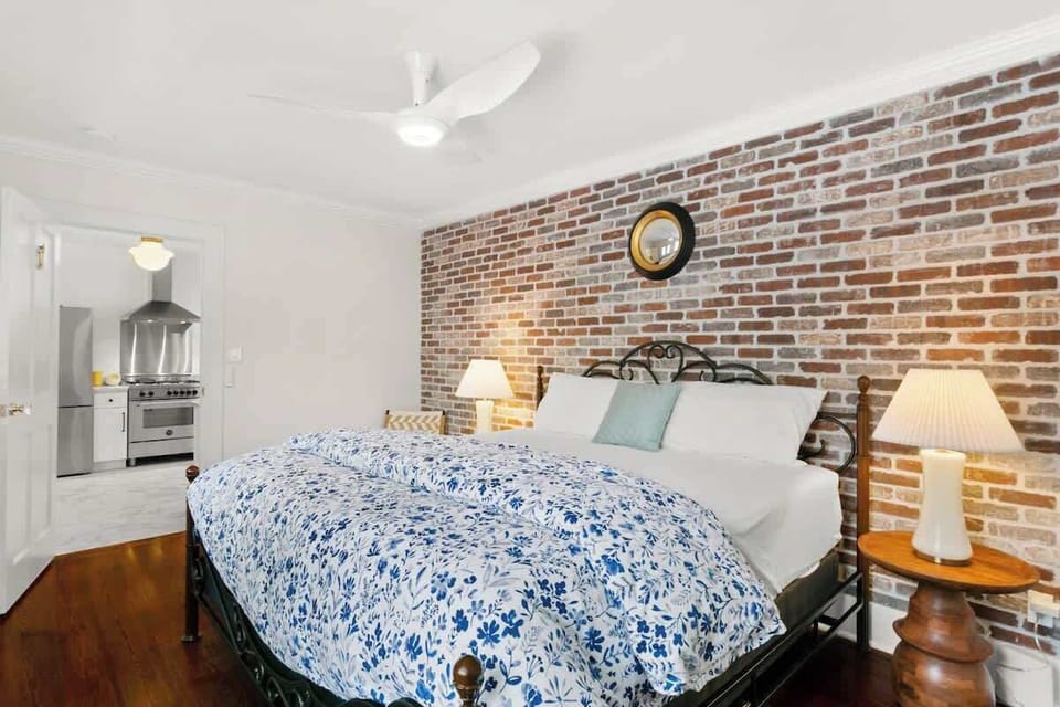Cozy bedroom with exposed brick, plush bedding, and warm lighting. Just off the kitchen, this inviting space offers comfort and New Orleans charm for a restful night after exploring the city.