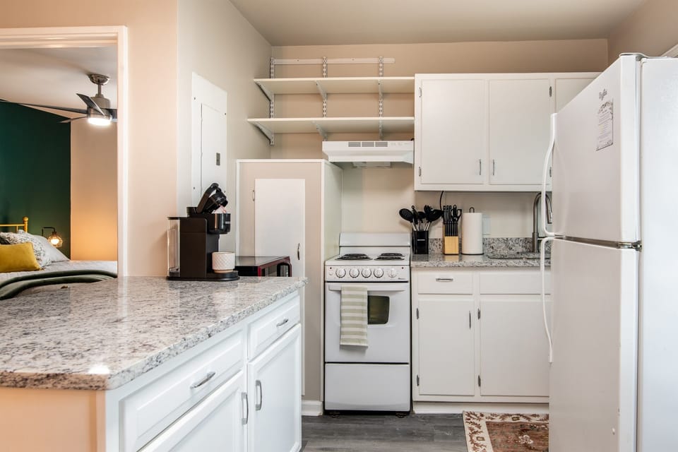 A compact and fully equipped kitchen with white cabinetry, granite countertops, and all essential appliances.
