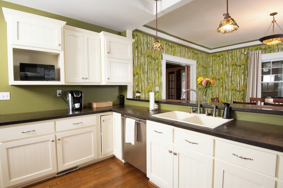 This full kitchen features a sleek two-door refrigerator, built-in oven, and stove. White cabinets provide a clean, modern look, beautifully contrasted by warm wood flooring, creating a bright and functional space perfect for cooking and gathering.