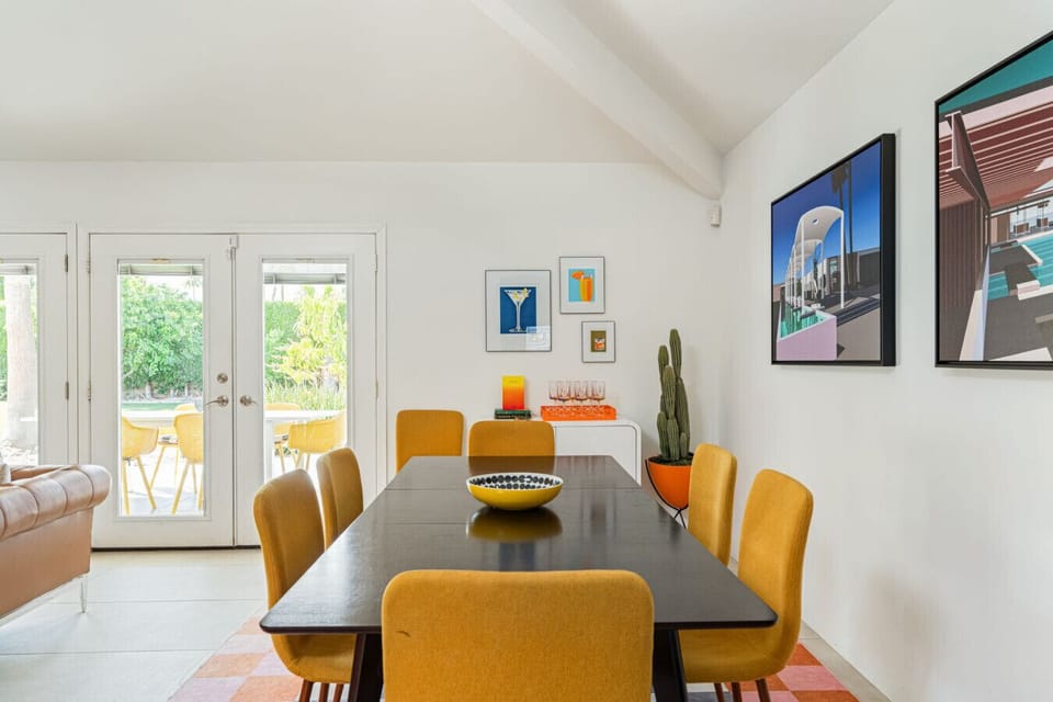 Sunny dining area w/ modern table, bright chairs, & French doors opening to the yard.
