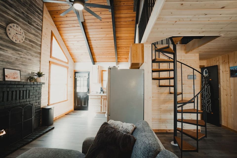 Cozy Cabin Charm – A view from the sofa showcasing the front entrance and spiral staircase leading to the loft bedroom. A perfect blend of character, charm, and a cool cabin vibe!