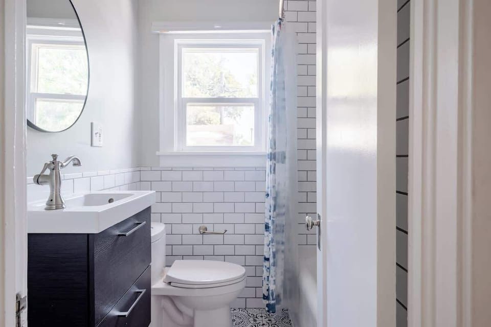 Bathroom with a sink vanity, toilet, shower curtain and visible shower fittings.