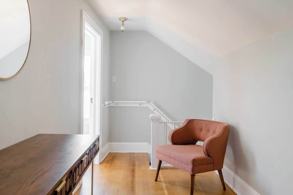 Desk and armchair beside a window and stairs.