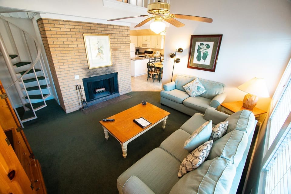 The cozy living room features a warm fireplace, comfortable seating, and a spiral staircase leading to a loft with twin beds, perfect for relaxing evenings in this peaceful 2-bedroom townhouse.